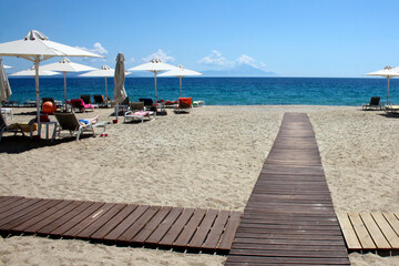 Beautiful seashore. Cloudless sunny day on a public beach. Umbrellas and sun beds are installed on the beach. The opportunity to relax and enjoy life. Athos, Macedonia (Greece), the Aegean Sea