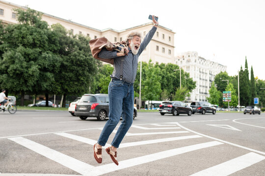 Excited mature man carrying luggage while jumping in joy on street