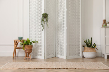 Folding screen and beautiful houseplants near white wall in room. Interior design