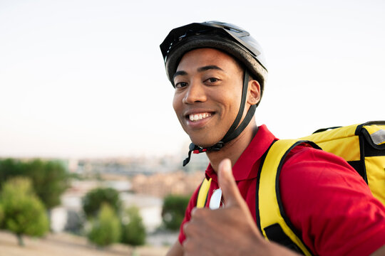 Smiling delivery man wearing helmet gesturing thumbs up