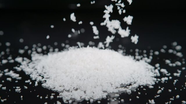 SLOW MOTION, MACRO, DOF: Tiny shreds of grated coconut fall down on the empty kitchen table. Shredded coconut meat flakes fall on the polished surface of a baker's countertop. Dessert ingredient.