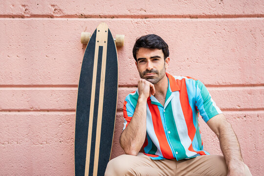 Handsome Man With Hand On Chin Sitting By Longboard