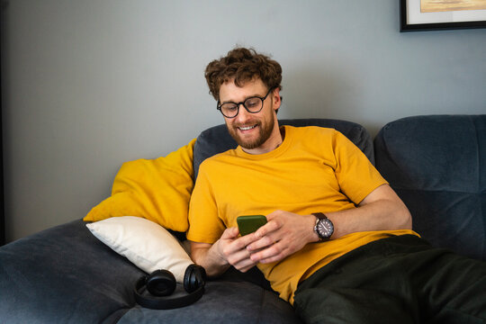 Smiling man using mobile phone while sitting on sofa at home