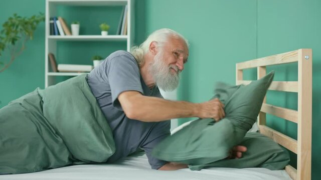 Elderly Man Tries To Rest, Gets Annoyed By Noisy Neighbors, Suffers From Insomnia On The Bed At Home. Thin Walls, Apartment Without Soundproofing, Renovation Work From Neighbors. Neighborhood Concept.