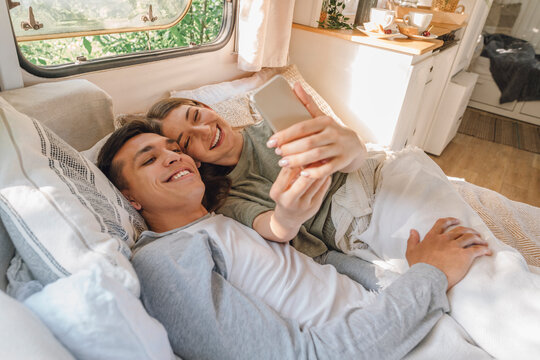 Happy woman taking selfie with boyfriend while lying on bed in motor home