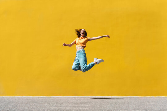 Cheerful woman with arms outstretched jumping on footpath