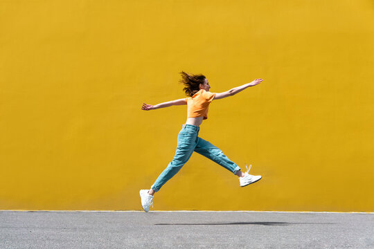 Playful woman with arms outstretched running on sunny day