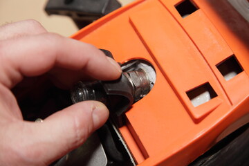 A man's hand removes the tip of a high-voltage wire from the spark plug of a chainsaw motor...