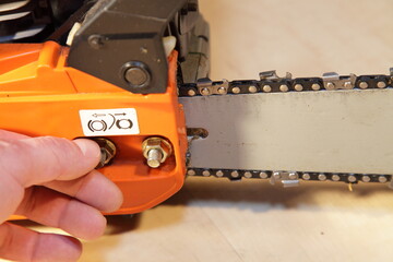 A man's hand check the chain tension on the chainsaw blade and holding the tension nut close up -...