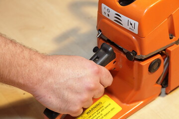 A man's hand holds the handle and pulls the chainsaw throttle trigger of the close-up - woodcutting tools equipment maintenance