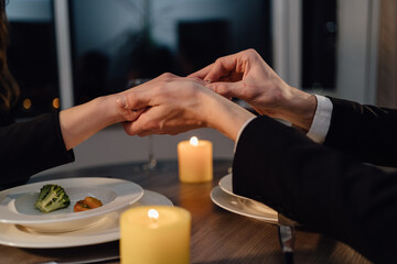 Obraz na płótnie Canvas man makes a marriage proposal to a girl in restaurant, put an engagement ring on a finger to a girlfriend, couple dinner on valentine's day