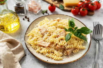 Pasta with ham in cream sauce in a ceramic plate on a light culinary background. Traditional Italian dish girandole in a bowl on the kitchen table close-up
