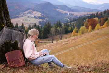 Fototapeta na wymiar Young woman drawing on tablet in mountains, space for text