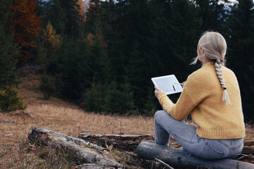 Young woman drawing with graphic tablet near forest in autumn
