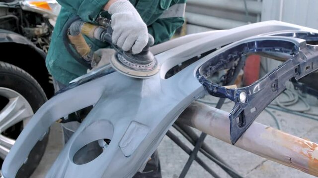 Worker In Gloves And Jumpsuit Cleans Surface Of Auto Bumper With Sanding Machine Professionally In Car Service Garage Before Painting Closeup