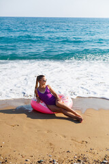 Fototapeta na wymiar Vacation at the sea. Beautiful slender woman in a swimsuit with an inflatable ring on the beach. Girl resting in the summer on the turkish coast
