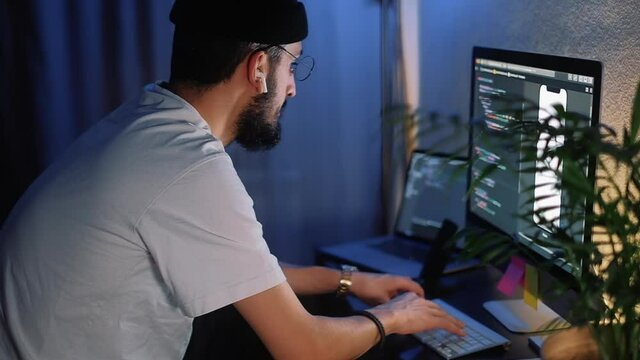 Young man mobile developer writes program code on a computer, programmer work in home office.