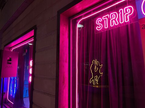 Pink neon sign of a strip club glowing