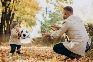 Fototapeta premium Father woth his little son in autumnal park playing with ball