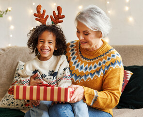 Happy afro american curly boy sitting on grandmother lap with christmas present, smiling at camera