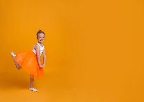 Cute little girl in tutu skirt dancing on orange background. space for text