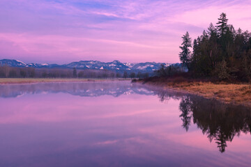 Obraz premium A purple and blue sunset illuminates a smooth lake and distant mountains on the horizon. The tranquil scene is in the Snoqualmie Valley of Washington State