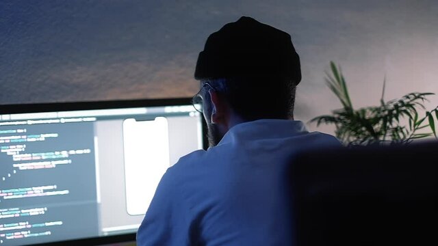 Young man mobile developer writes program code on a computer, programmer work in home office.