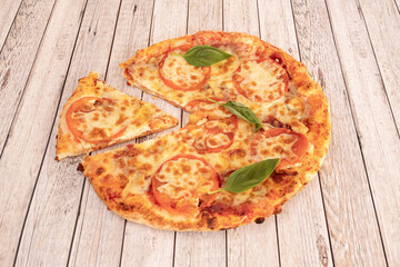 simple stone oven baked pizza with tomato, mozzarella cheese and basil with a separate slice