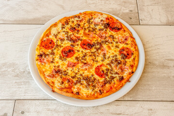 Cannibal Pizza with Bacon, Ground Beef, Pepperoni Slices and Lots of Mozzarella Cheese on a Round White Porcelain Plate
