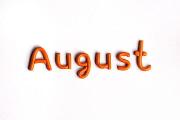 The word August is made of orange plasticine on a white background