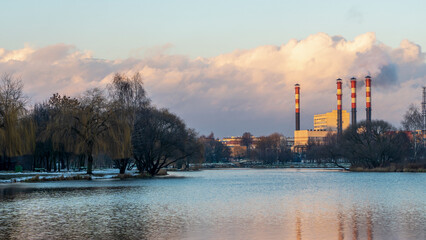 Smoking chimneys of thermal power plants near the waterfront in city. Winter. Industrial and nature background.