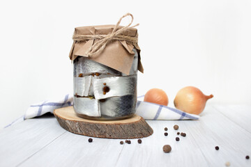 Pickled herring fish with pepper in jar on the table on light background