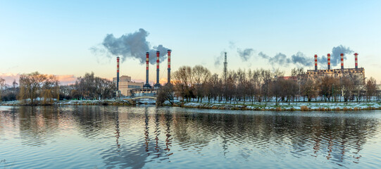 Naklejka premium Smoking chimneys of thermal power plants near the waterfront in city. Winter. Industrial and nature background.