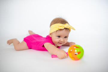 cute, beautiful little girl in a pink bodysuit
 and a bandage lies on a white background, smiles and gnaws toys. beautiful baby. teeth are erupting. portrait of a baby. portrait of a beautiful girl