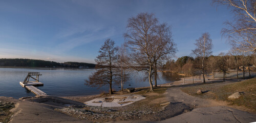 Pale Winter solstice reflex in the calm lake Mälaren, beach with jump tower and life saver at an...