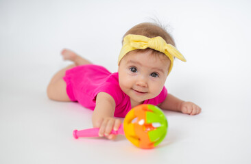 Fototapeta na wymiar cute, beautiful little girl in a pink bodysuit and a bandage lies on a white background, smiles and gnaws toys. beautiful baby. teeth are erupting. portrait of a baby. portrait of a beautiful girl