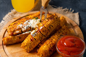 Grilled corn on the cob with barbecue spices and sauce, served on a wooden board.