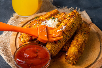 Appetizing grilled corn in spices close-up greased with a brush with butter.