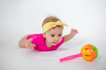 cute, beautiful little girl in a pink bodysuit
 and a bandage lies on a white background, smiles and gnaws toys. beautiful baby. teeth are erupting. portrait of a baby. portrait of a beautiful girl