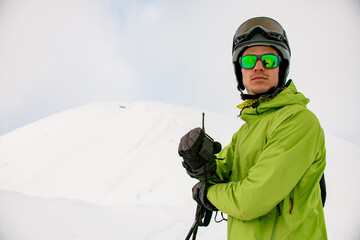 man in sunglasses and ski helmet holds walkie-talkie in his hand against background of white snow