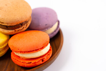 Multicolored macarons on a wooden plate on a white background.