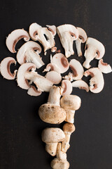 Cut champignon and some mushrooms tree-shaped on a black wooden table 