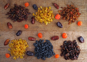 Wooden background with heaps of raisins of various varieties, dates and kumquats.
