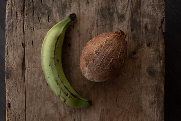 Green banana and brown coconut on old wood