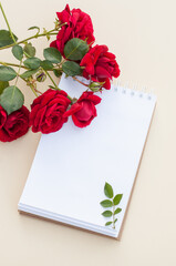 red roses are lying next to a clean paper notebook on a spring on a light background