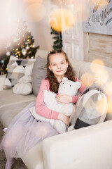 Portrait of a young girl in a New Year's house. She is sitting on a sofa with soft pillows . The lights of the Christmas tree shine behind
