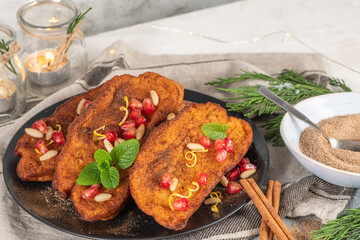 Traditional Christmas Rabanadas with lemon zest, pomegranate, pine nuts and cinnamon. Spanish Torrijas or french toasts close up on the countertop