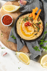 Delicious hummus in ceramic bow lwith  carrot stick dipped in hummus. Colorful snack composition on a white background.