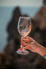 A female hand holds a glass of wine against the background of the sea and mountains.