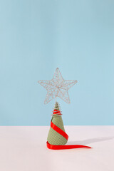 Christmas tree made of green ice cream cone wrapped in red ribbon with silver star bauble on top. Blue pastel colored background, close up perspective. Christmas and new year celebration concept.
